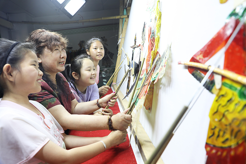 皮影藝人指導(dǎo)小朋友表演皮影戲。